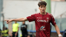 a young man in a soccer uniform is pointing at something while playing soccer on a field .