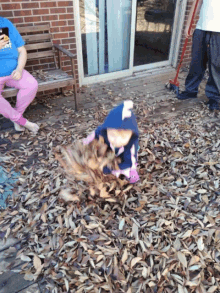 a little girl is playing in a pile of leaves while a woman sits on a bench in the background