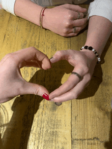 a couple making a heart shape with their hands on a wooden table