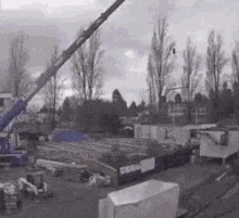 a black and white photo of a construction site with a crane in the foreground and trees in the background .