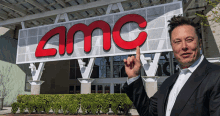 a man in a suit stands in front of a large amc sign