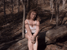 a woman sitting on a log in the woods with her legs crossed