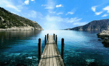 a wooden dock leading into the ocean with mountains in the background .