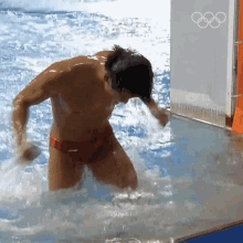 a man in red swim trunks is standing in a pool with the olympic rings on the wall behind him