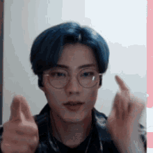 a young man with blue hair and glasses is making a heart shape with his hands .