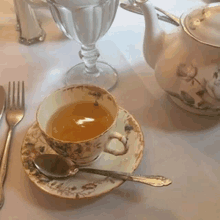 a cup of tea sits on a saucer next to a spoon and fork on a table .