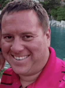 a man in a pink shirt is smiling in front of a pool