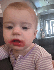 a baby with red lipstick on his face is wearing a purple and white striped shirt