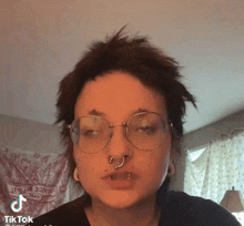 a woman wearing glasses and a nose ring has a tiktok icon next to her face