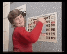 a young boy in a red sweater is standing in front of a wall with a poster on it .