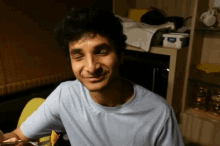 a man in a blue t-shirt is smiling in front of a shelf with a container of yogurt on it