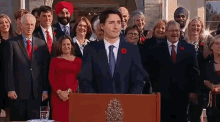 a man in a suit and tie is standing at a podium with a group of people behind him .