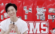 a young man is smiling in front of a wall of red lockers with the word ms on them .