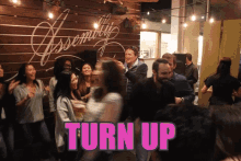 a group of people are dancing in front of a wall that says " turn up "