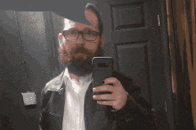 a man with a beard and glasses takes a selfie with his phone