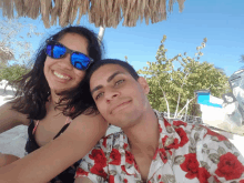 a man and a woman are posing for a picture under a thatched umbrella