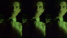 a man in a suit and tie is standing in the dark with a green light shining on his face .