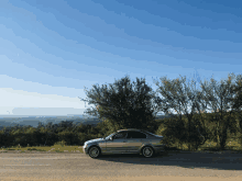 a silver car is parked on the side of the road with trees in the background