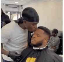 a man is kissing another man 's forehead while getting his hair cut .