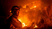 a man wearing a helmet stands in front of a large fire