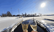 a person is holding two glasses of wine in front of a snowy field