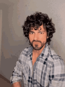 a man with curly hair and a beard in a plaid shirt