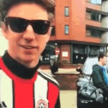 a young man wearing sunglasses and a red and white striped shirt is standing in front of a building .