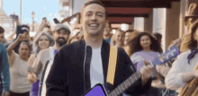 a man playing a guitar in front of a crowd with a purple guitar that says ' ukulele ' on it