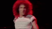 a man with red hair is wearing a white shirt and dancing on a stage .