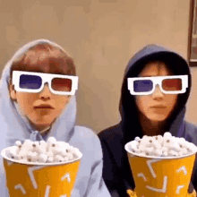 two people wearing 3d glasses are eating popcorn and watching a movie .