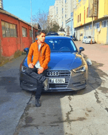 a man sits in front of a blue audi with a license plate that says kj 6984