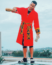 a man in a red robe is pouring a bottle of champagne into a pool