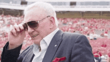 an elderly man wearing sunglasses and a suit is sitting in a stadium .