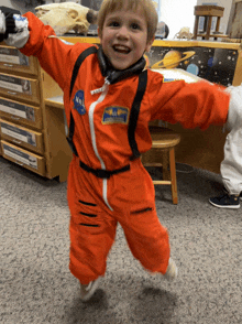 a young boy dressed in an orange nasa space suit is smiling