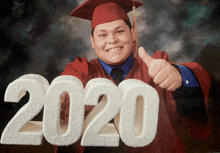 a man in a graduation cap and gown is giving a thumbs up in front of a sign that says 2020