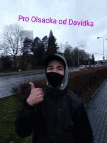 a man wearing a mask giving a thumbs up in front of a sign that says pro olsaca od davidka