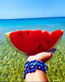 a person holding a slice of watermelon in front of a body of water