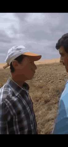 two men are standing in a field and one is wearing a hat