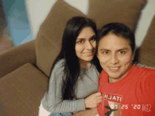 a man and a woman are posing for a photo and the man is wearing a red ajjati shirt