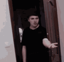 a man in a black shirt is standing in front of a door with his hand out .