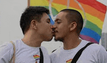 two men are kissing each other in front of a rainbow flag .