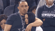 a man wearing a dallas cowboys football shirt is hugging a woman