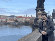 a man wearing a hat and scarf leans against a wall overlooking a body of water