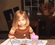 a little girl is sitting at a table with a pink cup and a spoon and making a face .