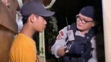 a man in a baseball cap and glasses is talking to a police officer while holding a walkie talkie .