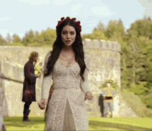 a woman in a white dress with a flower crown on her head stands in front of a stone wall