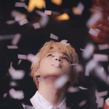 a man in a white shirt looks up at confetti falling around him