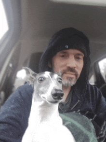 a man in a hooded jacket is holding a small white dog