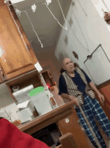 a man with a cane is standing in a kitchen with a green pitcher