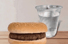 a hamburger and a glass of water on a wooden table